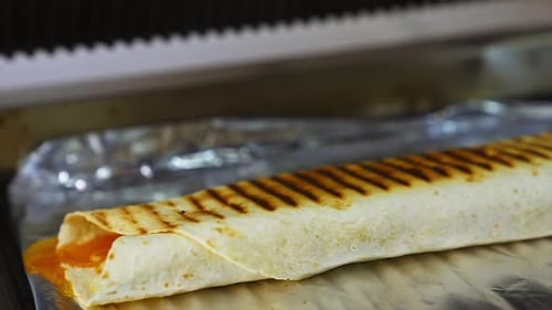 Cheese shawarma with vegetables lies on a foil. Grilled pita with ingredients. Close up.