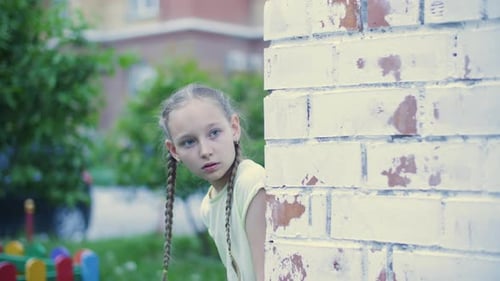 Adolescente assustada espiando da esquina da casa de tijolos no bairro residencial. Garota preocupada