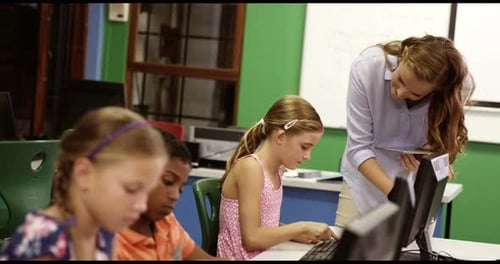 Teacher assisting school kids on personal computer in classroom