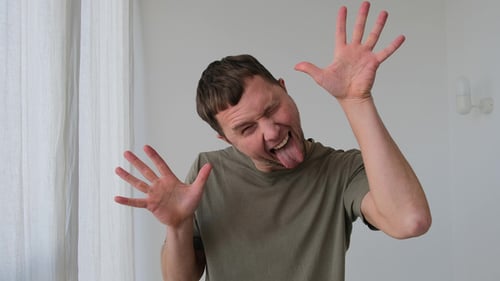 Playful Man in Tshirt Shows Tongue and Gestures in Room