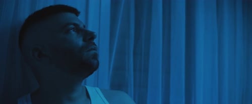 Close up of a depressed man sitting on a bed, staring at the ceiling.