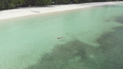 Aerial: woman swimming in turquoise water at sunset white sand beach tropical coastline