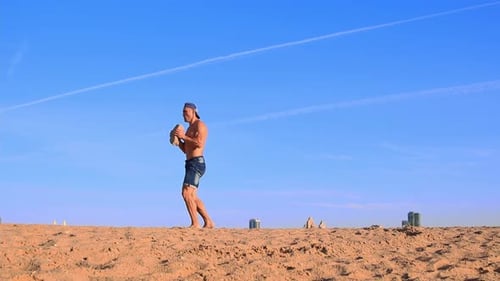 Young Fit Man Doing Sports Exercises at the Beach Holding a Heavy Rock in His Hands Doing Small
