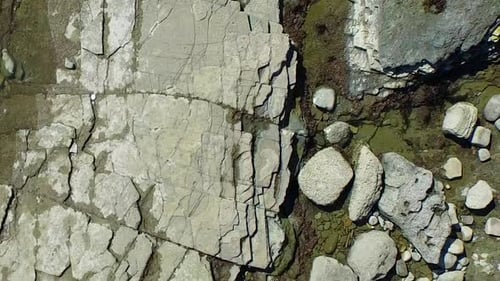 Aerial birds eye view shot of a young man running on a rocky ocean beach shoreline.