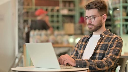 Professioneller junger Mann benutzt Laptop im Café