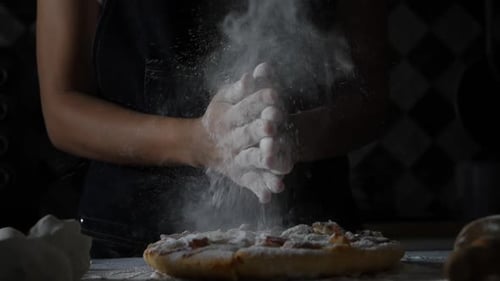 Zeitlupe von Frauenhänden, die Mehl auf Pizza sieben