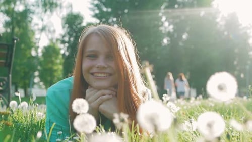 Beautiful Young Woman with red hair lying on the field in green grass and dandelion. Outdoors. Enjoy