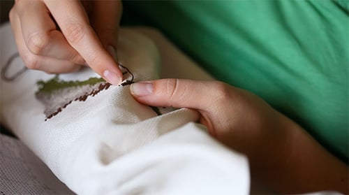 Hands Embroidering Delicate Design on White Fabric