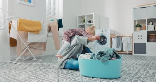 Playful Child Hugging Mother Doing Laundry at Home