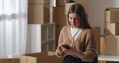 Warehouse with Cardboard Boxes in Apartment Woman Is Using Smartphone Communicating with Clients