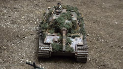 Eine Ausstellung von Automodellen der Armee. Ein getarnter Panzer fährt und dreht auf einer vorbildlichen unbefestigten Straße.