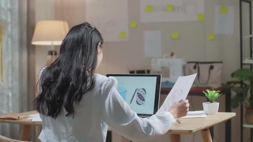 Vista posterior de un diseñador de bolsos de mujer con tela mirando el lazo de diseño mientras usa la computadora portátil