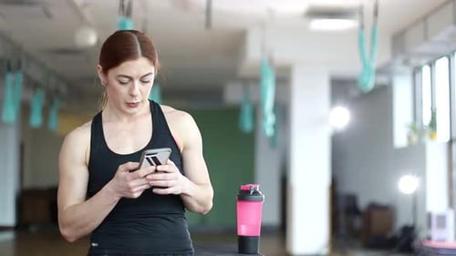 Fitness woman drinks water after a workout, fitness model rests in the gym