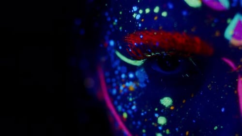 Jeune femme au maquillage fluorescent brillant qui brille sous la lumière UV. Gros plan de son œil qui s'ouvre et se ferme