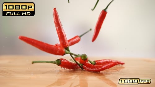 Red Chili Peppers Falling onto Wet Wooden Table