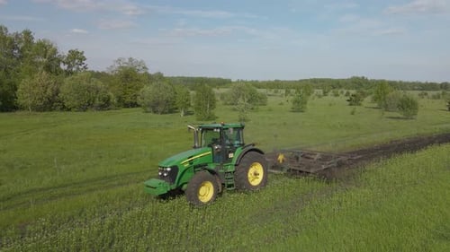 A rural tractor drags a plow across a field with rising dust