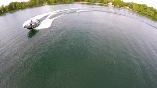 Aerial birds-eye drone view of a man wakeboarding behind a boat.