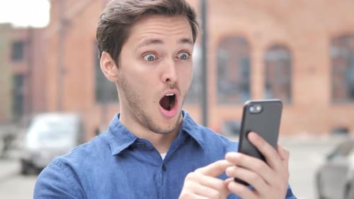 Excited Young Man Using Smartphone in City