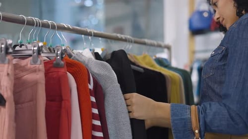 Female Customer Makes Purchases in Clothing Store Chooses Stylish Clothes Hanging on Rack Hangers