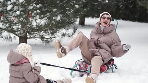 Young Happy Mother and Her Daughter Enjoying a Sledge Ride in a Beautiful Snowy Backyard