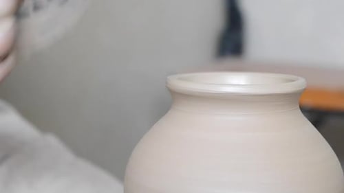 Hands Shaping Pottery with a Tool