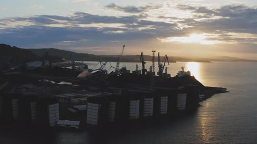 Silhouetten von Frachtkranen, die am frühen Morgen in der Morgendämmerung im Hafen arbeiten