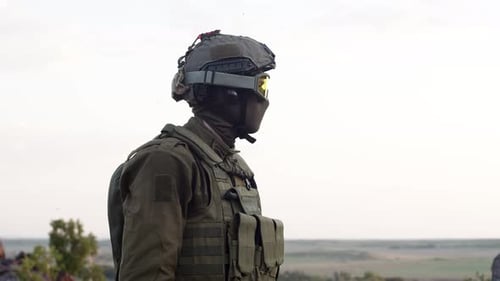 Serious Confident Sniper Man Stands Sideways in Field Turns His Head in Helmet and Talking on the