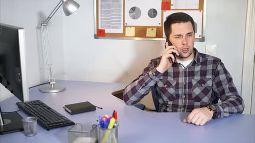 Businessman Is Negotiating on Smartphone in His Office Where There Is a Computer