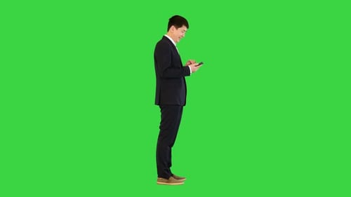Asian Man in Suit Smiles While Using Mobile Phone on a Green Screen Chroma Key