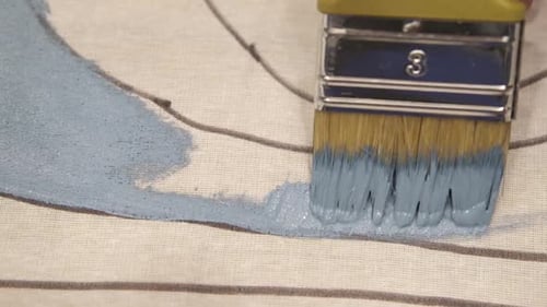 Paint Brush Applying Light Blue Paint to Canvas