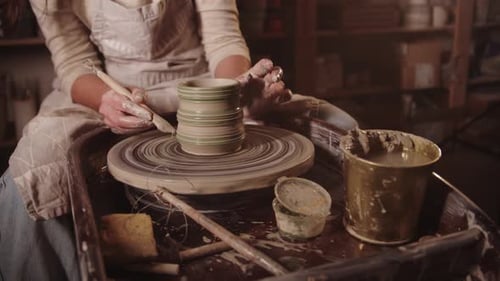 Young Woman Potter Makes Faces on a Wet Clay Pot Using a Tool