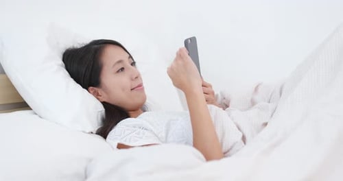 Woman Using Phone Relaxing in Bed at Home