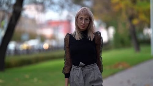 Confident Blonde Townswoman Is Strolling in Park at Early Autumn Day, Looking at Camera, Medium
