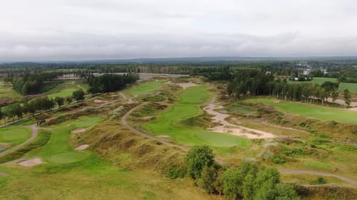 Aerial birds eye view of golf course on a cloudy day, situated near a woody area.