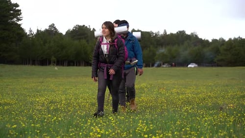 People Hike in Grassy Field With Backpacks