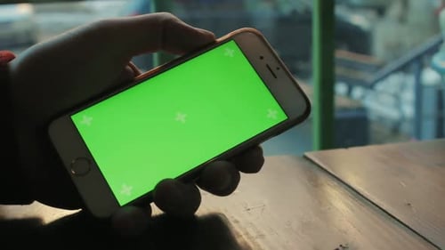A Man a Cafe at the Wooden Table Uses the Phone with Green Screen