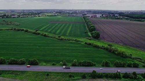 Cars Driving on Asphalt Road Along the Green Fields in Rural Landscape