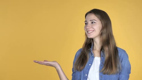 Smiling Woman Presenting with Open Hand on Yellow