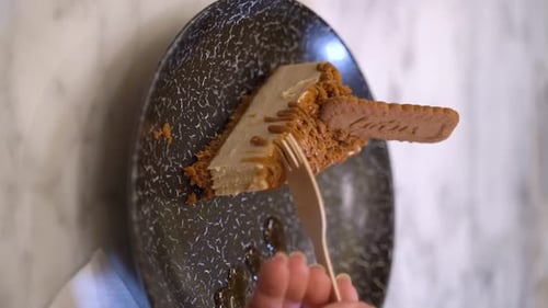 Enjoying Cheesecake with Biscuit Crumbles and Wooden Fork