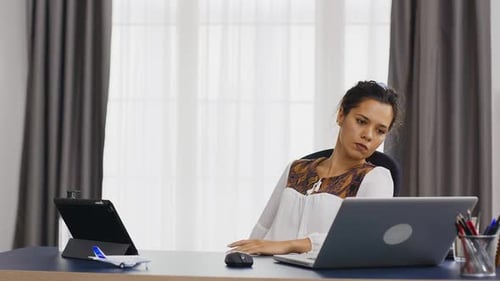 Woman Stretches Neck at Desk in Home Office
