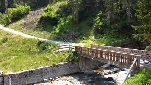 Aerial shot chasing a women mountain biking past a bridge in a mountain forest