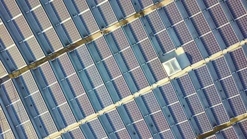 Aerial view of many photo voltaic solar panels mounted of industrial building roof.