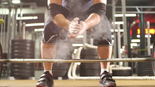 Young Bodybuilder Preparing To Lift Heavy Barbell in Modern Gym Hall, Hands in Talc
