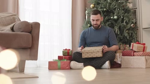 Man Opening Christmas Presents at Home on Floor
