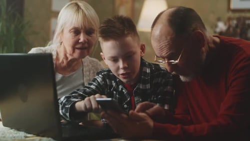 Boy Showing Phone to Grandparents at Table Indoors