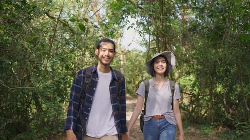 Young Asian man and woman friend or couple traveling walking with happiness in the forest together.