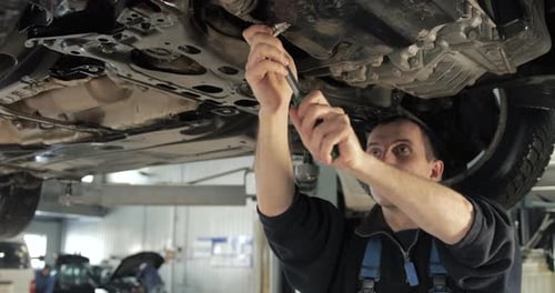 Car Mechanic Repairing Vehicle Underside in Garage