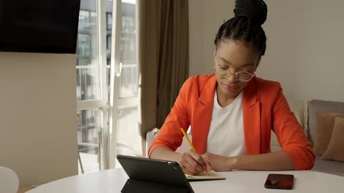Young Adult African American Woman is Studying Using a Video Call Noting Down the Lesson