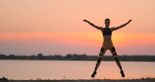 Woman Doing Jumping Jacks at Sunrise by Water