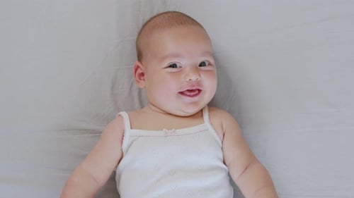 A Nice Little Caucasian Newborn Baby Is Funny Smiling, Lying at the Back in the Child Crib. Portrait